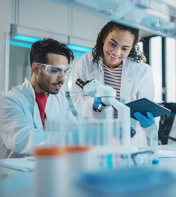 Forskare i laboratorium som arbetar med mikroskop i FoU‑miljö, symboliserar forskning, utveckling och teknisk innovation.